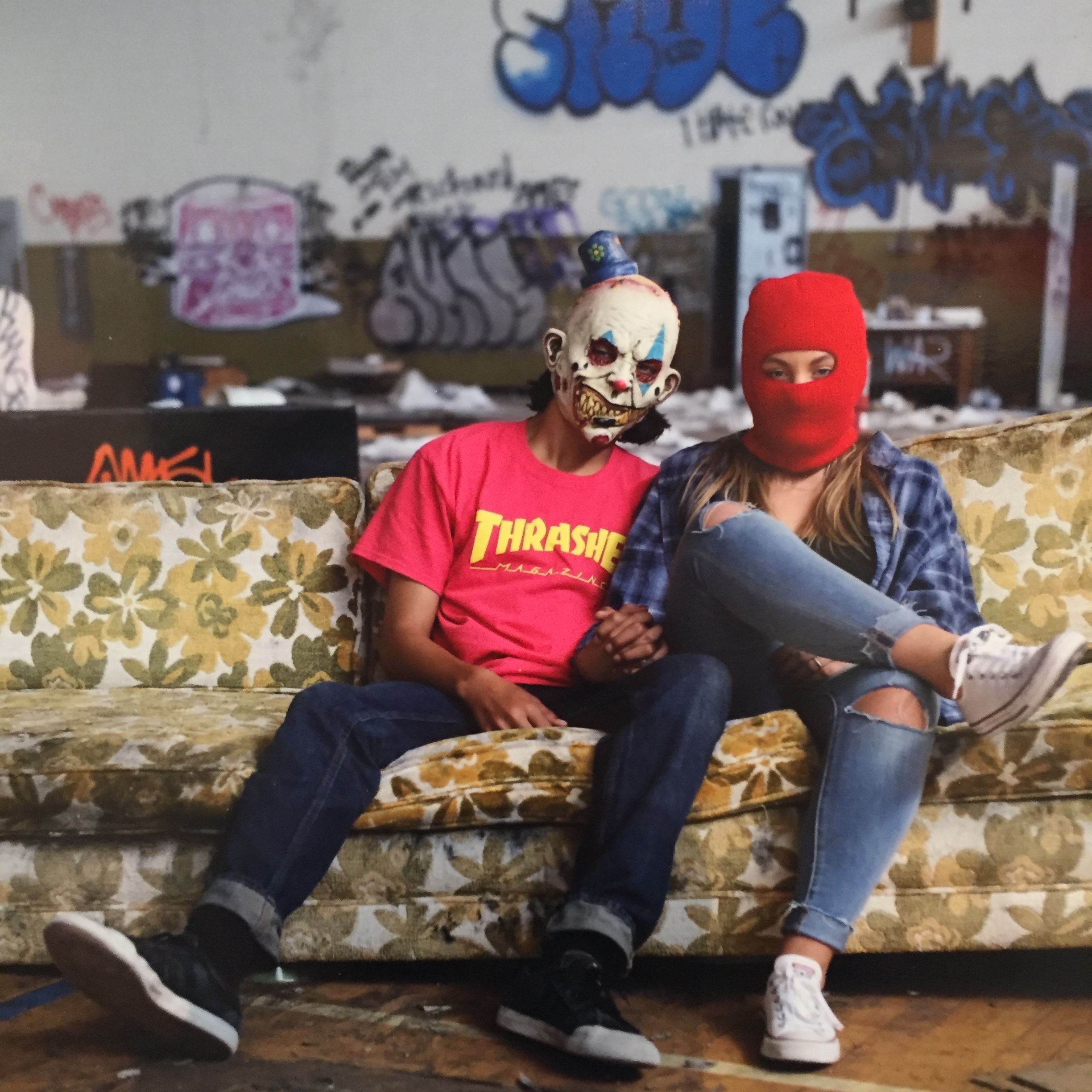 Photograph of two masked people on couch surrounded by graffiti
